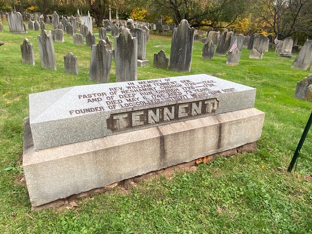 A gravestone in a cemetery commemorating Rev. William Tennent, a pastor from the 18th century and founder of a college, surrounded by other headstones.